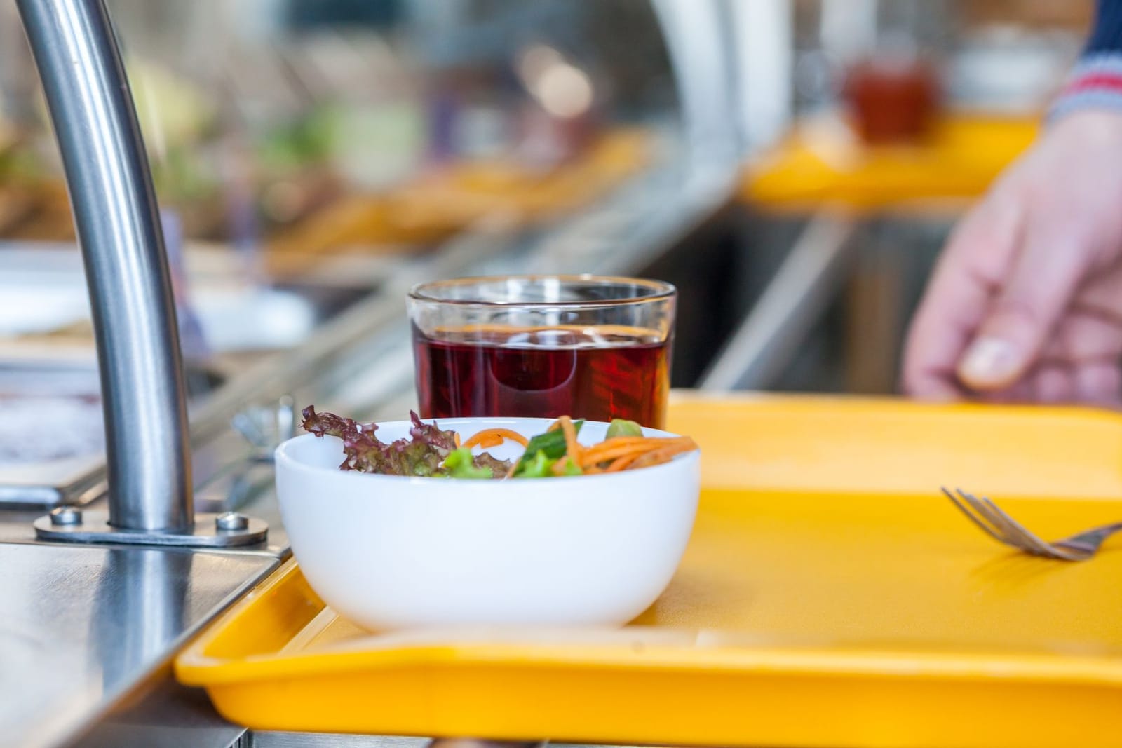 A cafeteria tray with a salad bowl, fruit juice and fork on a canteen counter