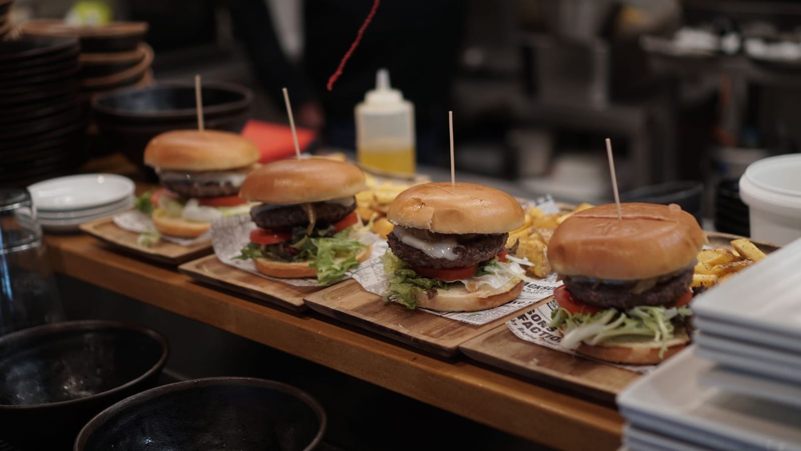 Rangée de burgers façon smash avec pains toastés et frites sur des planches en bois dans une cuisine londonienne