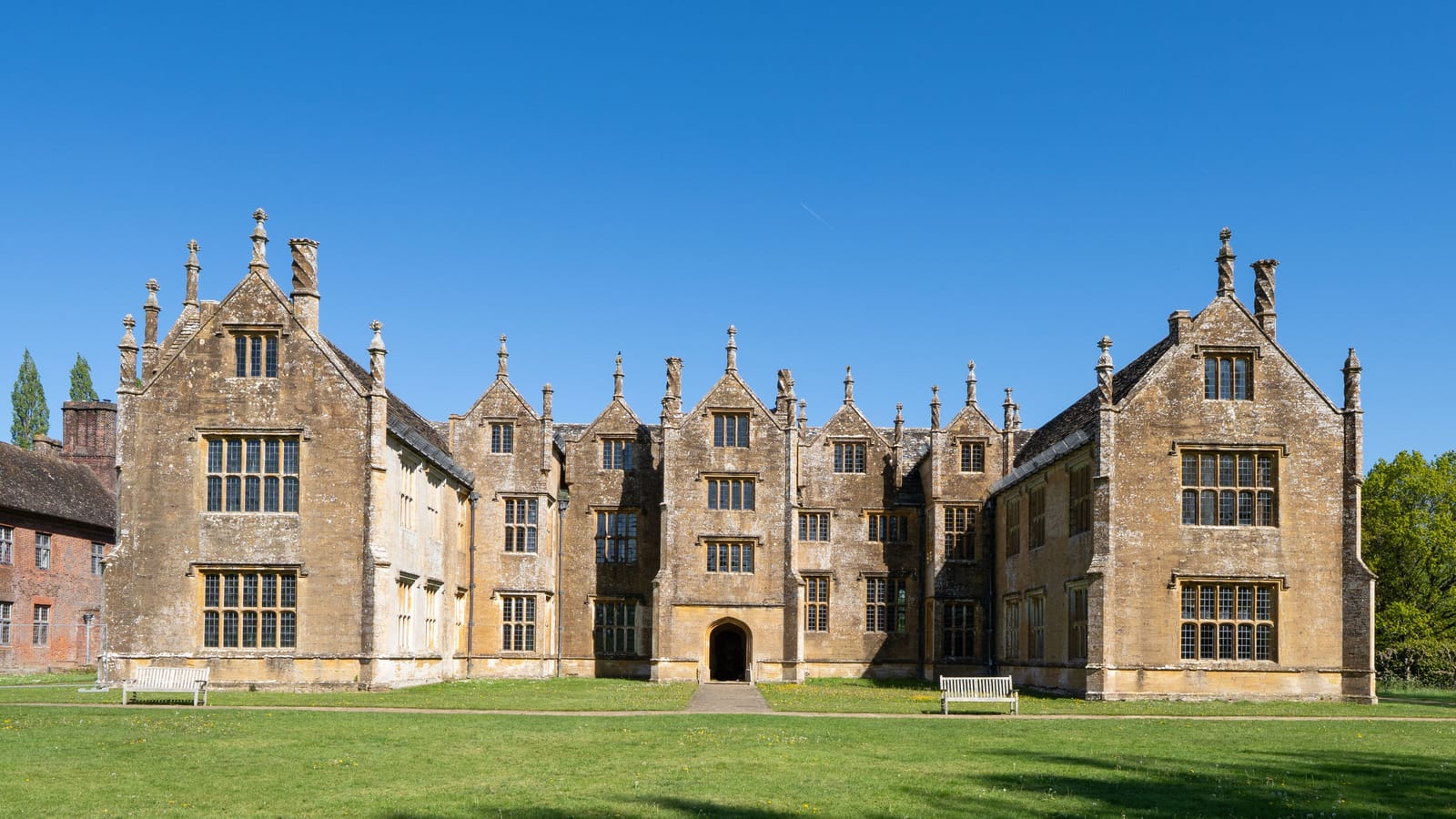 Historic English stone manor house with gabled roofline under a clear blue sky