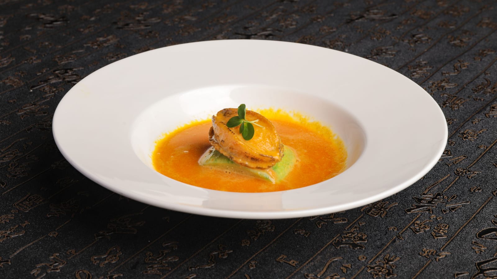 Elegant fine-diningbord met een gebakken hapje in oranje saus op een donkere tafel