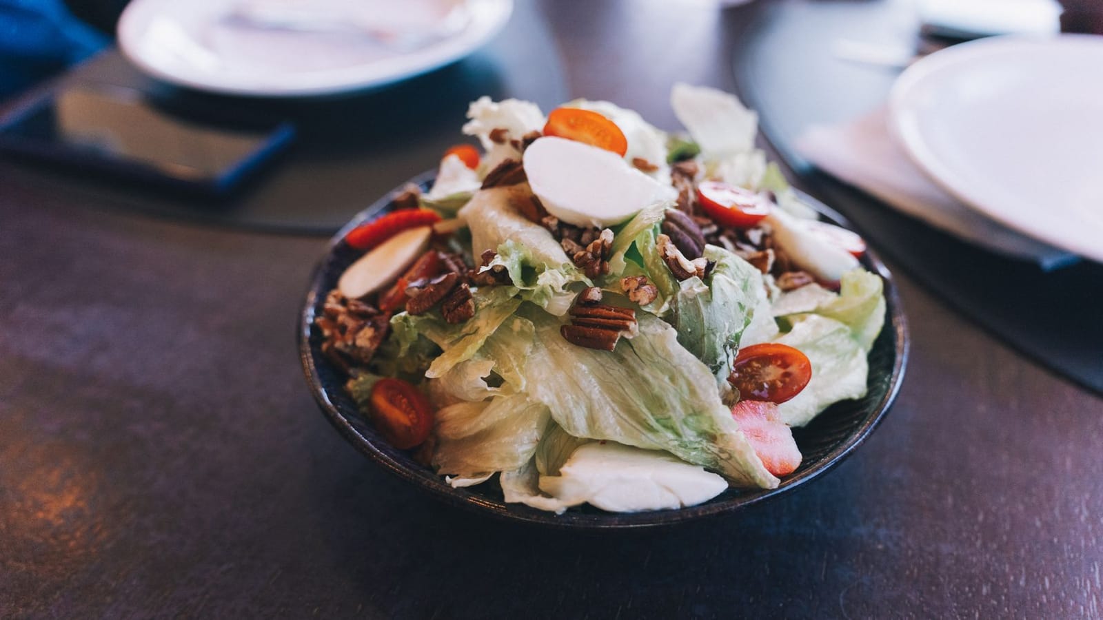 Insalata mista con pomodorini, noci pecan e mozzarella fresca su un piatto scuro