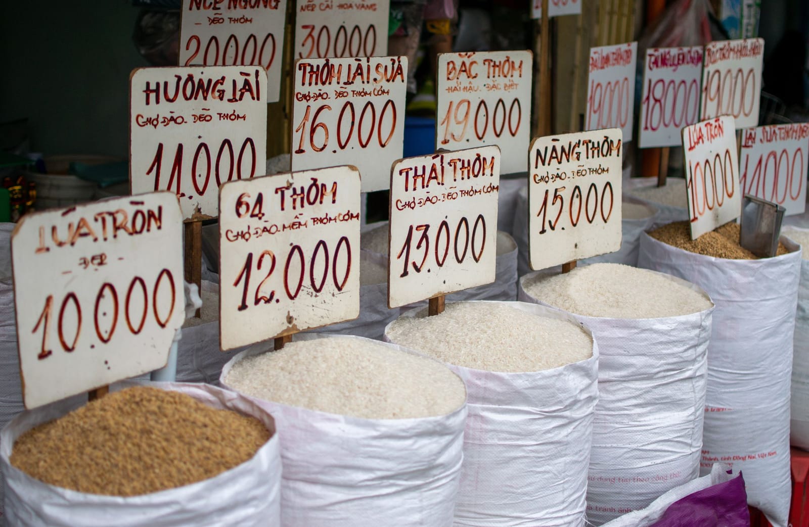 Open sacks of rice at a market stall with handwritten price signs on each variety
