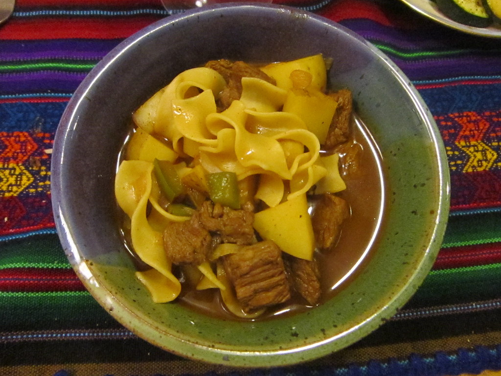 Bowl of goulash with beef, potato and egg noodles on a striped woven cloth