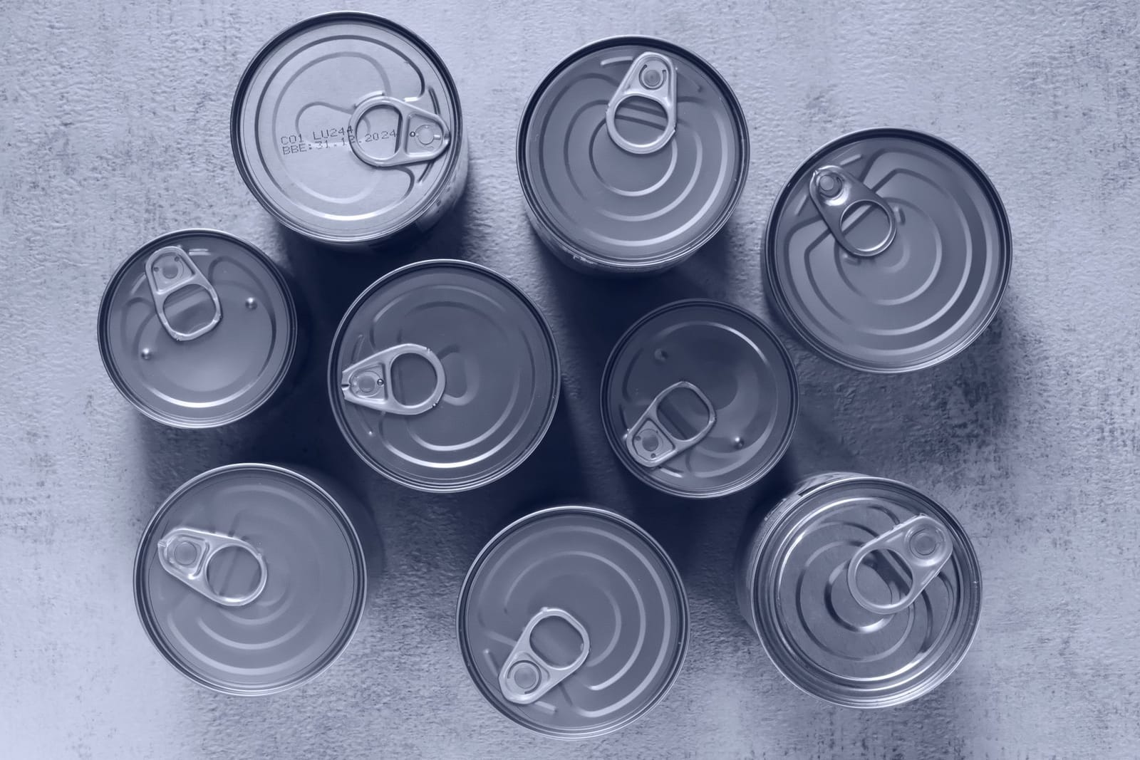 Unlabelled metal food cans with ring-pull lids seen from above on a grey surface