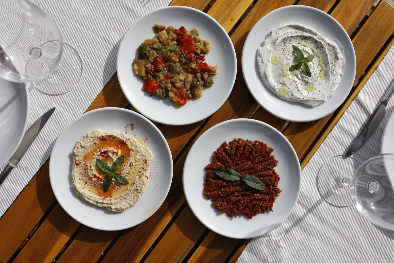 Bovenaanzicht van vier Griekse en mediterrane dips in witte kommen op een houten tafel