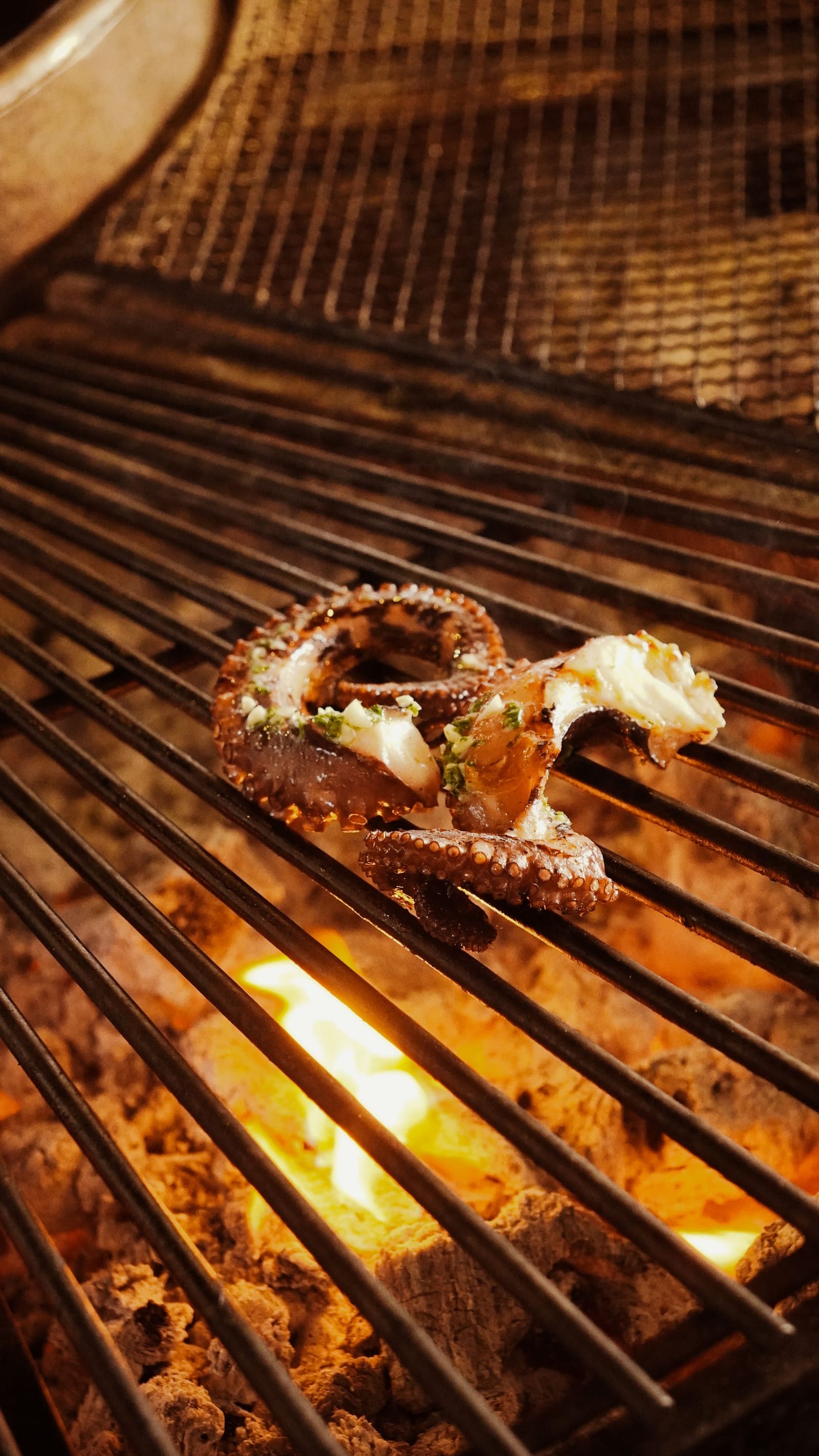 Octopus tentacles charring over an open flame on a restaurant grill