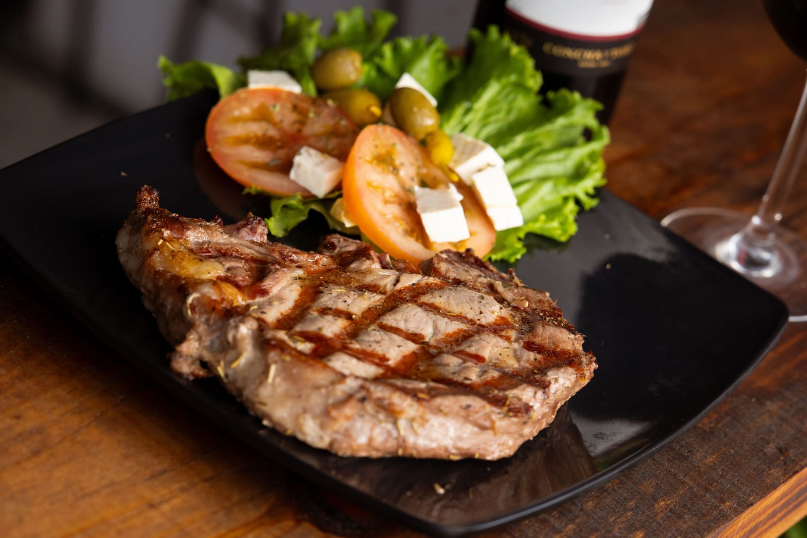 Gegrilltes Steak mit Salat und Feta neben einem Glas Rotwein