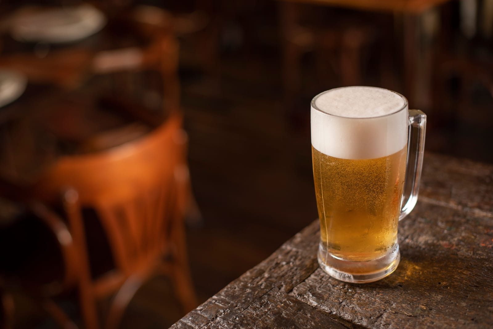 Een volle pint lagerbier met een dikke schuimkraag op een versleten houten pubtafel