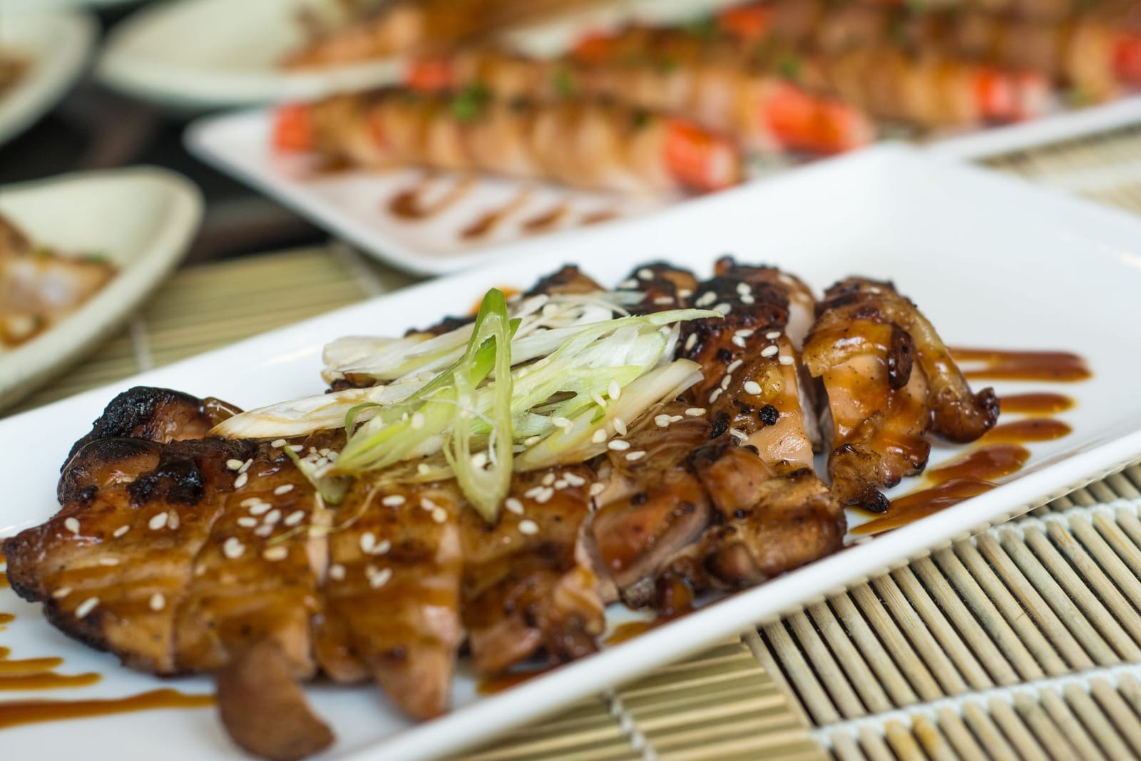 A grilled Japanese robata dish with charred chicken skewers and scallion garnish plated on a white rectangular dish