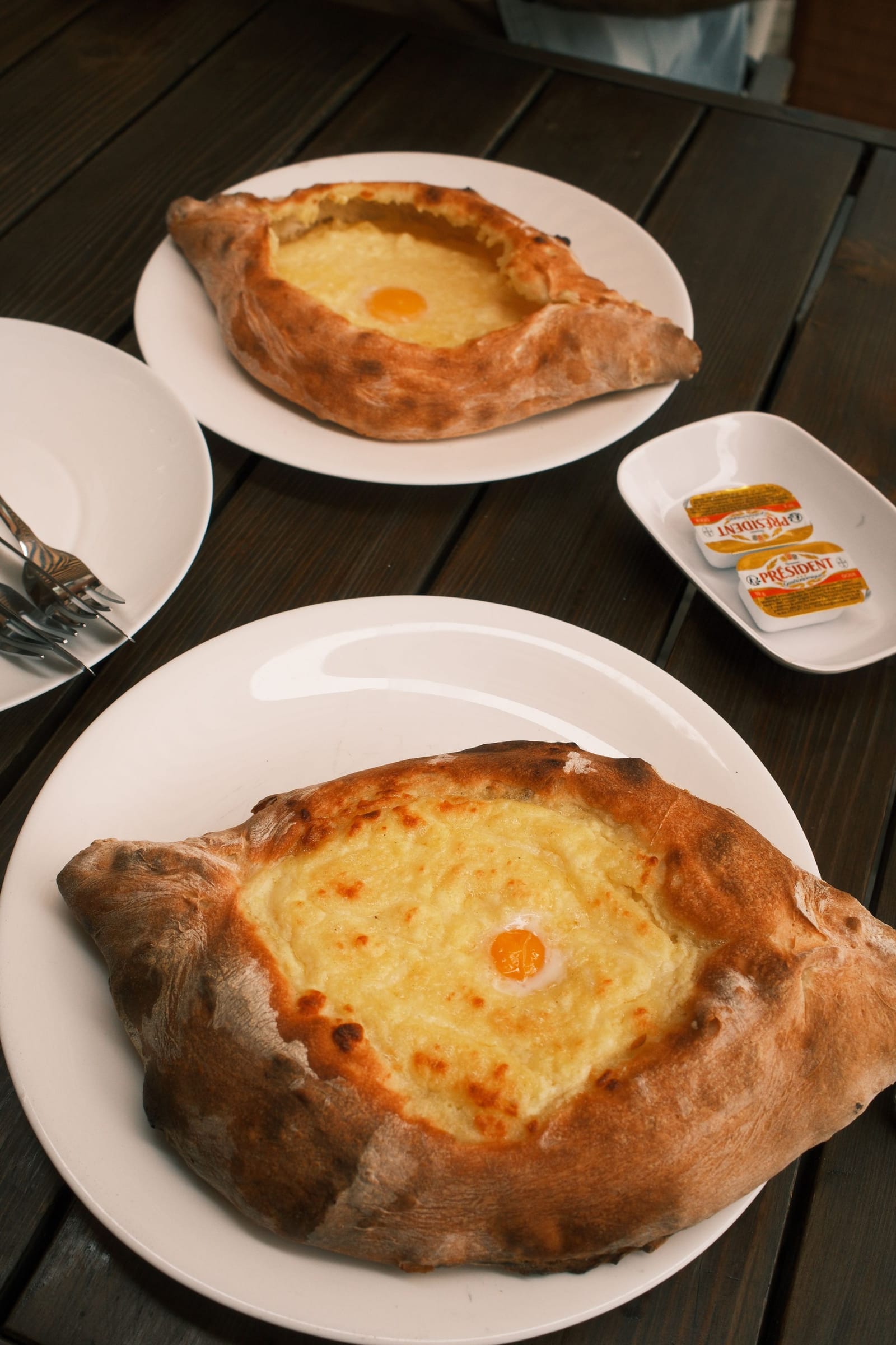 Two freshly baked khachapuri with a cracked egg yolk on top, on a wooden table