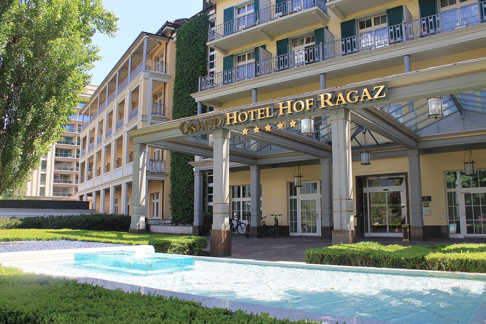 Ingresso del Grand Hotel Hof Ragaz con una fontana e siepi in primo piano