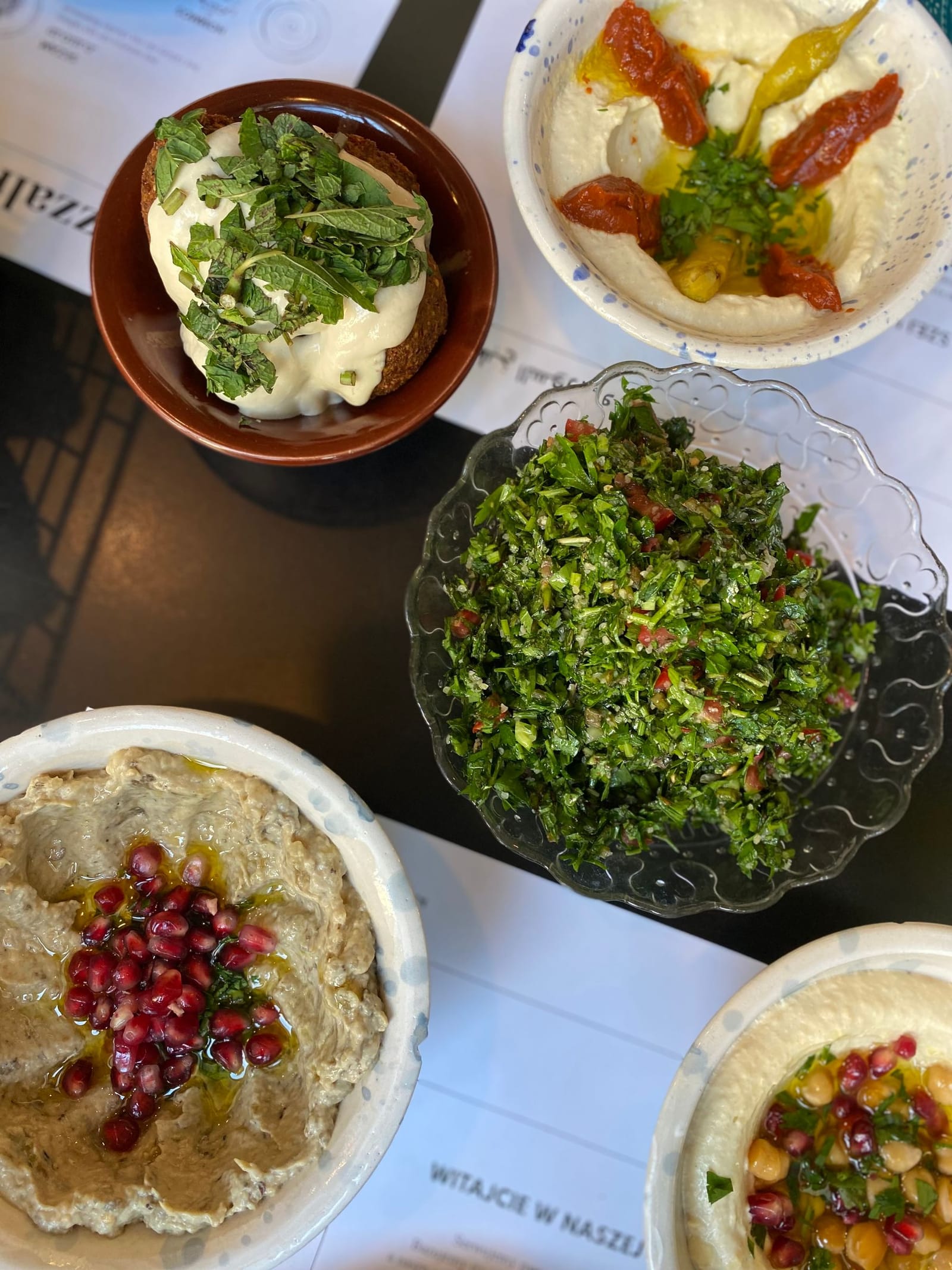 Overhead view of hummus, baba ganoush, tabbouleh and falafel bowls on a restaurant table