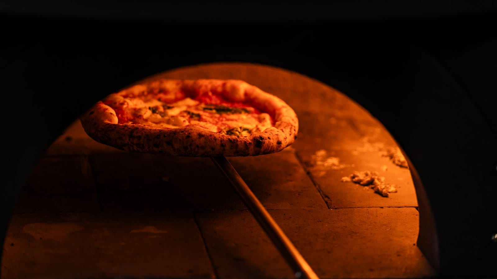 Een Napolitaanse margherita pizza op een houten schep in een gloeiende houtoven