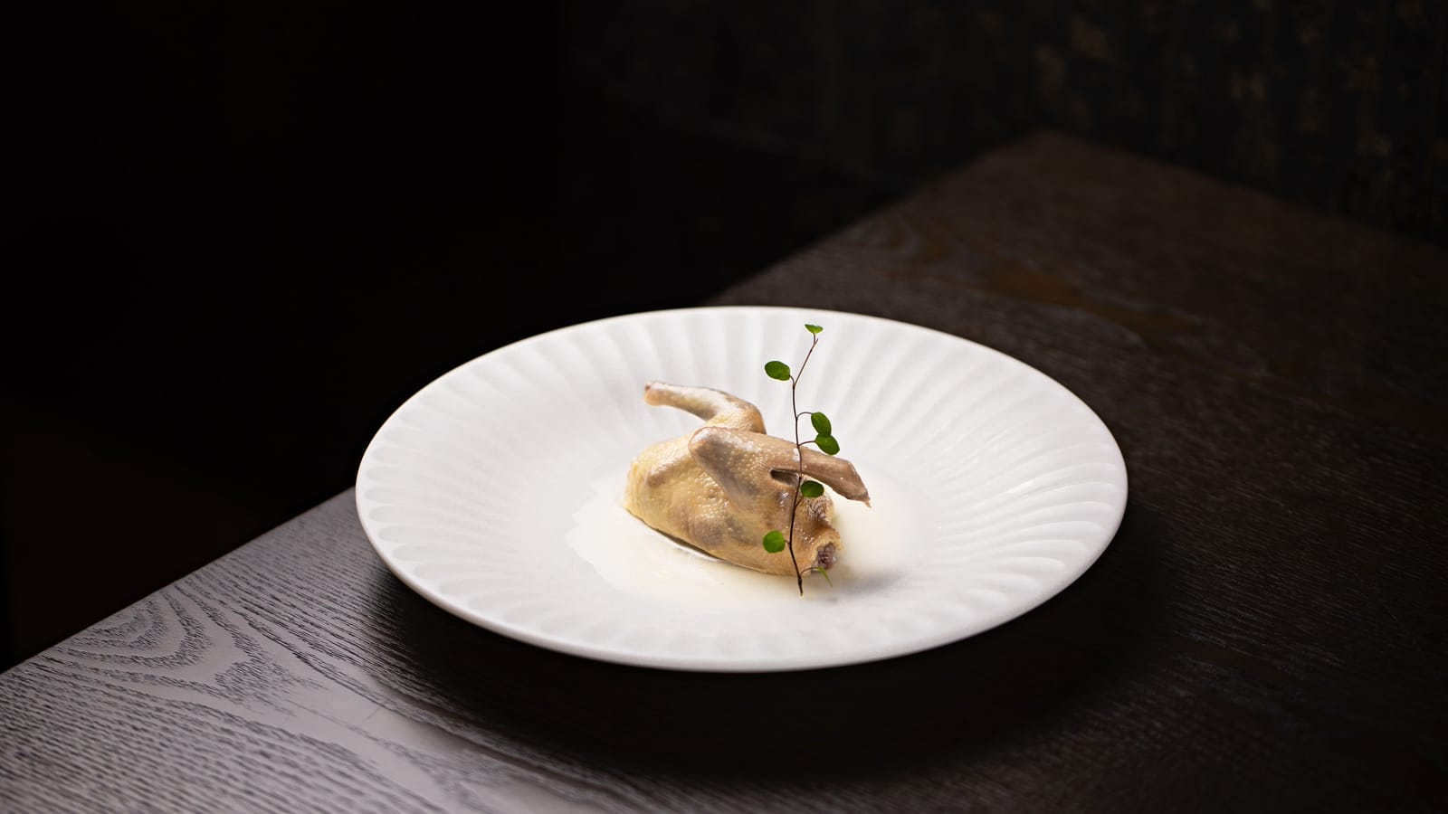 Un plat minimaliste dressé sur une assiette blanche cannelée dans un restaurant gastronomique italien