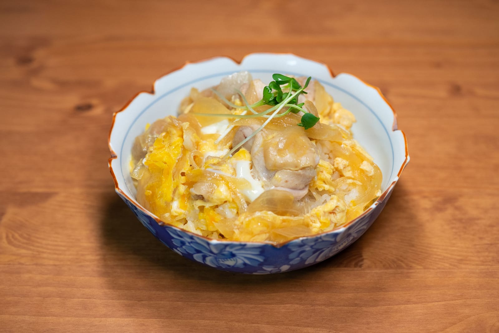 Ciotola di ceramica con oyakodon, pollo e uovo lucido rappreso, cipolla ed erbe sul riso