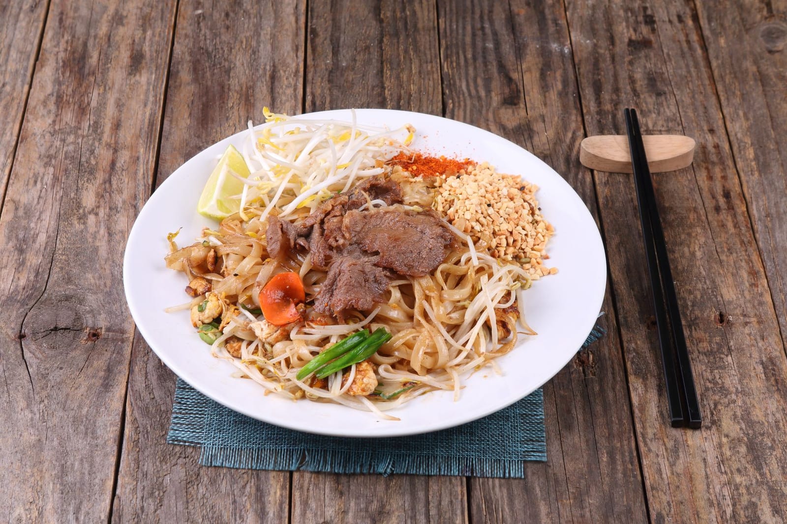 Beef pad Thai noodles with peanuts, lime and bean sprouts on a wooden table