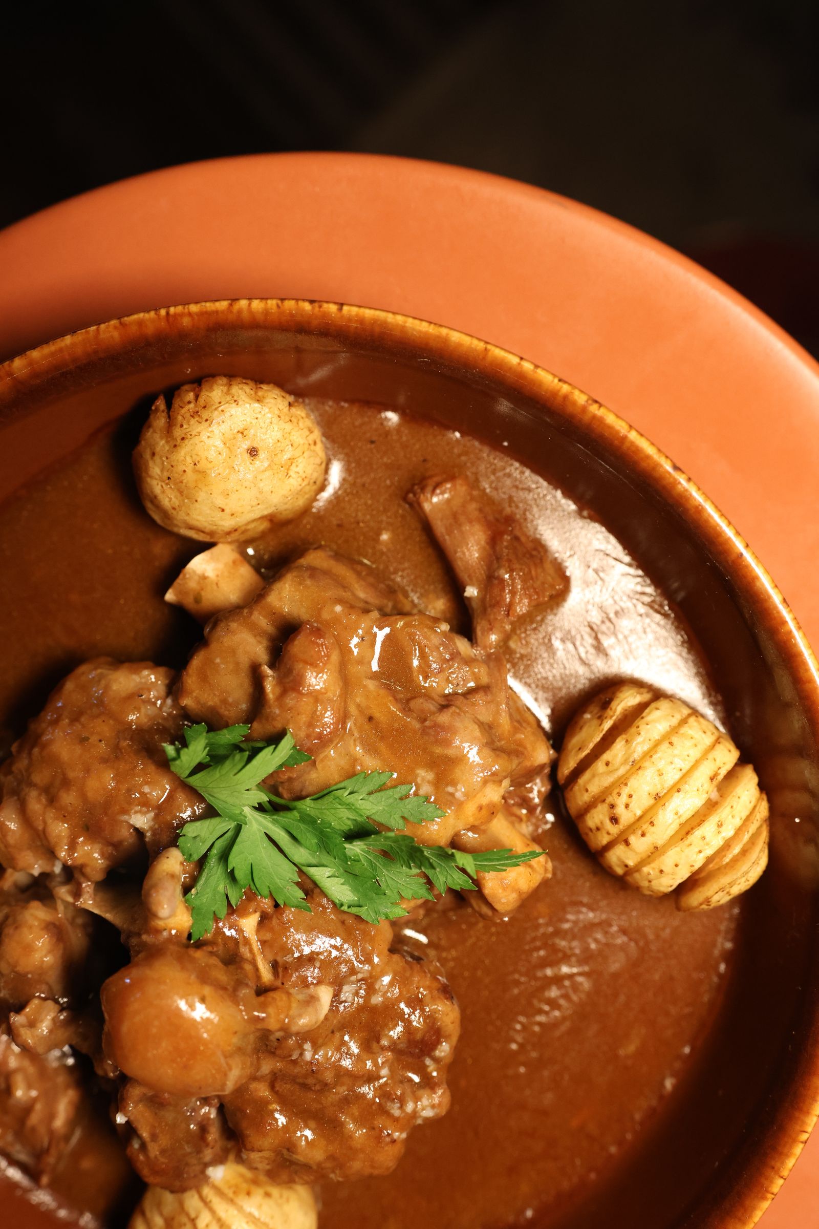 Close-up of a terracotta bowl filled with potato and chorizo stew garnished with parsley