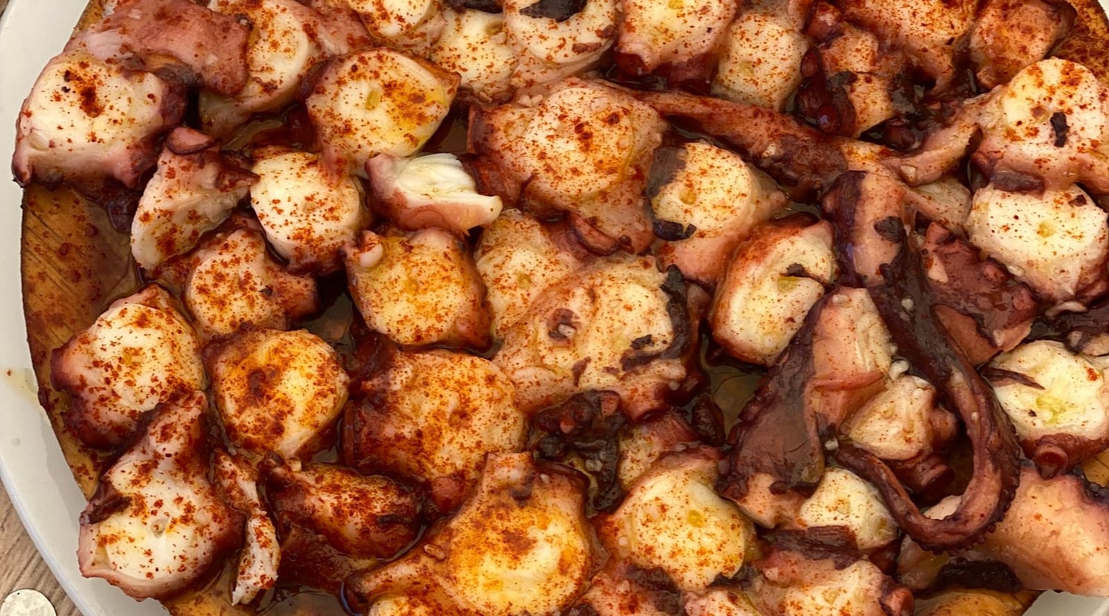 Galician-style octopus sliced on a wooden plate, dusted with paprika and coarse salt