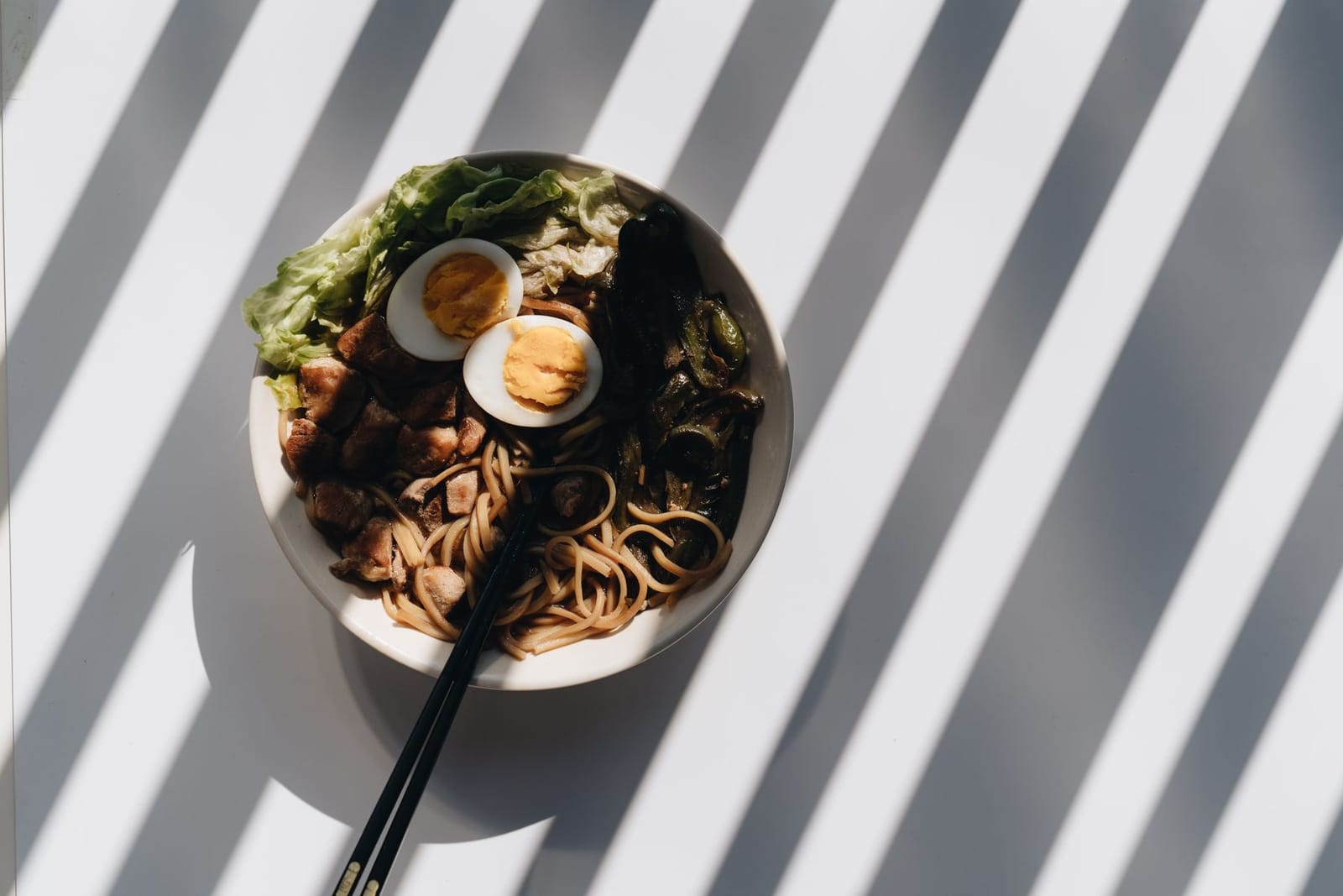 Overhead ramen bowl with eggs, pork and scallions in dramatic light