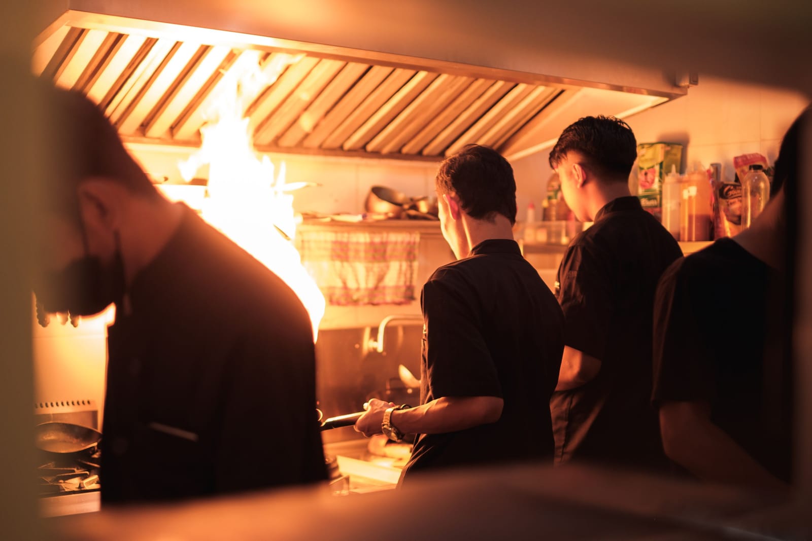 Personal de cocina trabaja codo con codo junto a una llama abierta en una cocina profesional concurrida