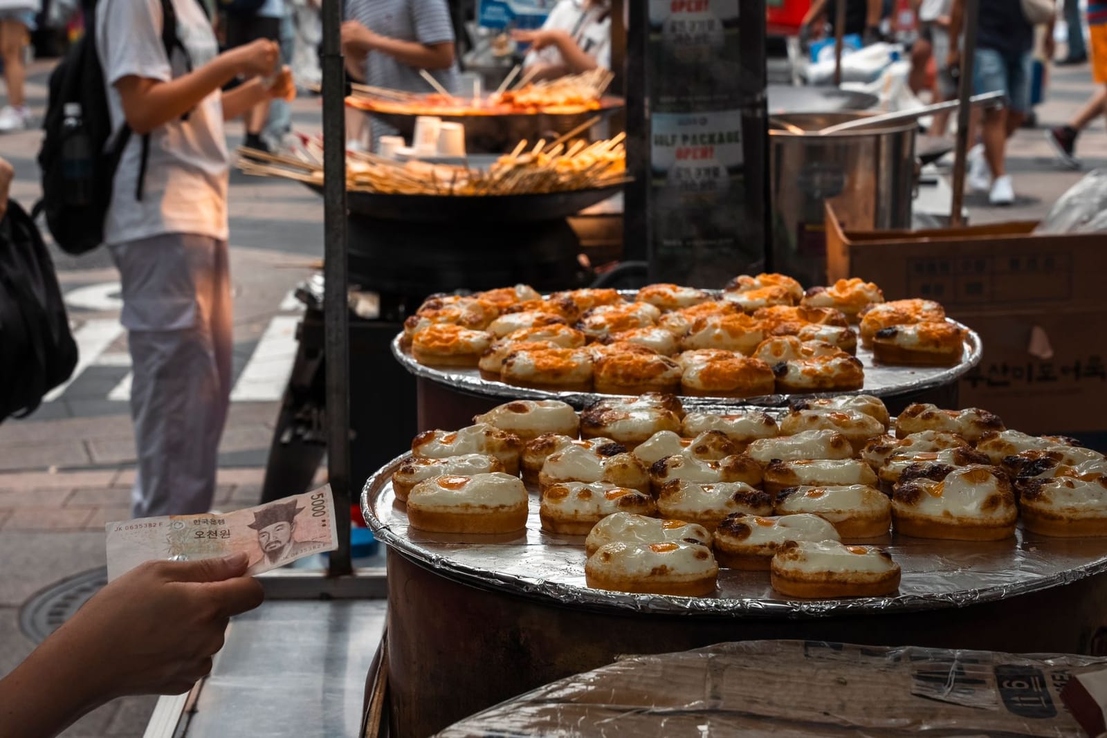 Un stand de street food à Séoul rempli de petits pains aux œufs grillés, un vendeur servant un client qui paie en wons coréens