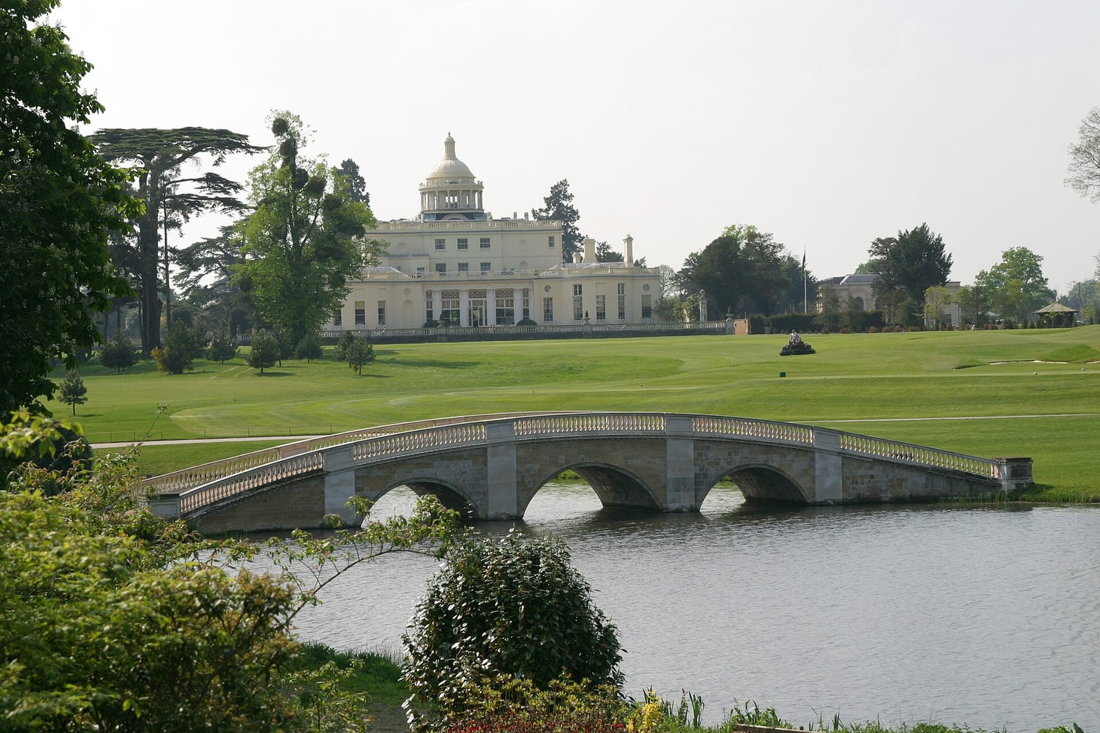 Het landhuis van Stoke Park met witte koepel achter een stenen brug over het meer