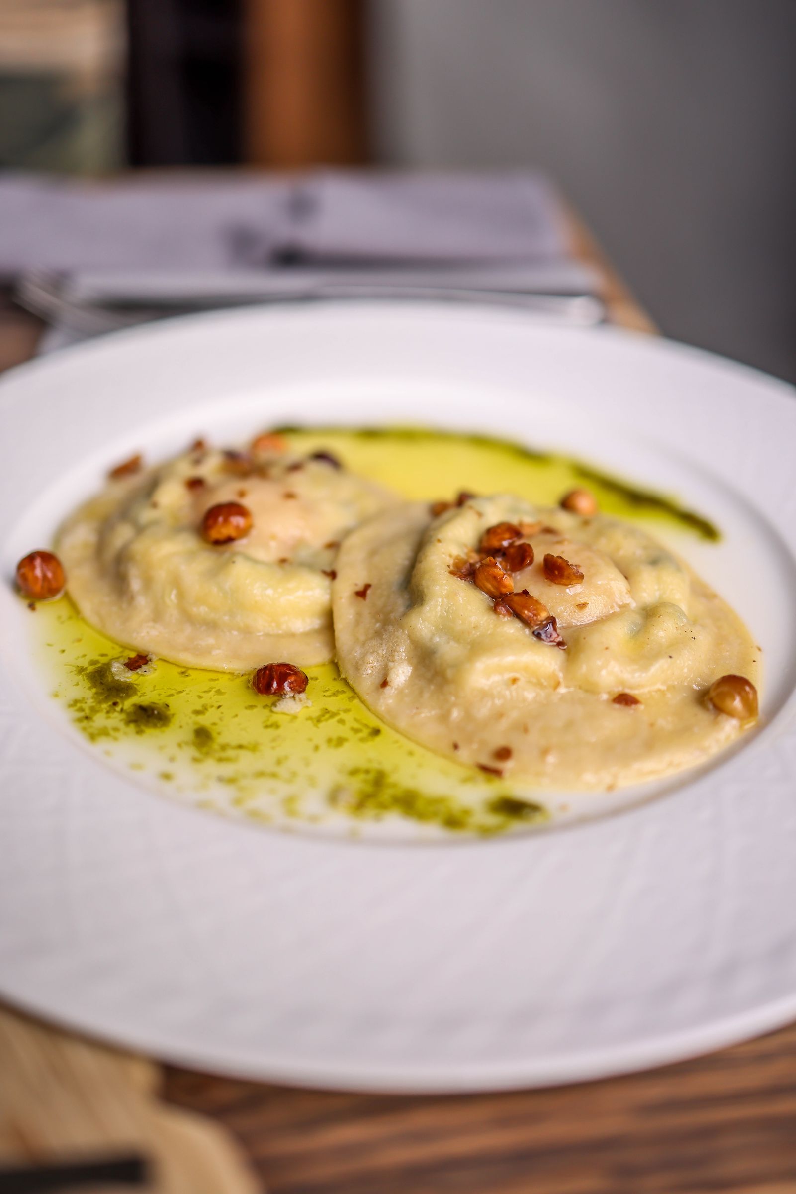 Due tortelli di zucca su un piatto bianco con burro dorato, nocciole e salvia