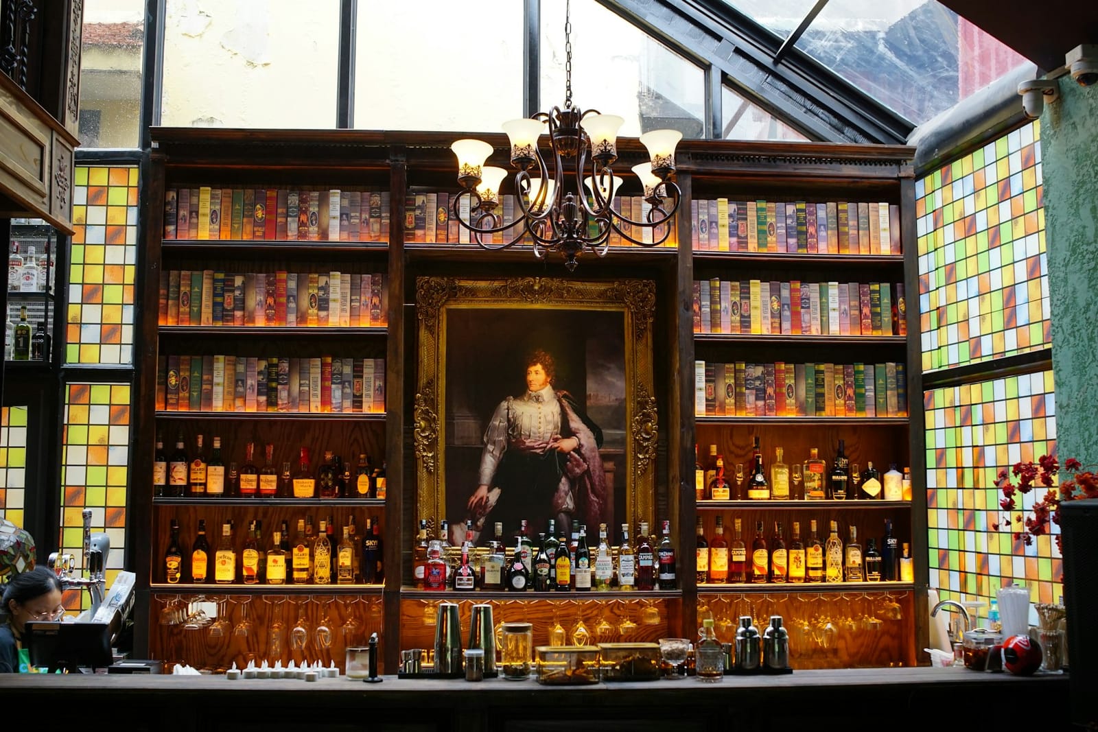 Un bar de cóctel de estilo vintage con botellas, libros y un retrato con marco dorado