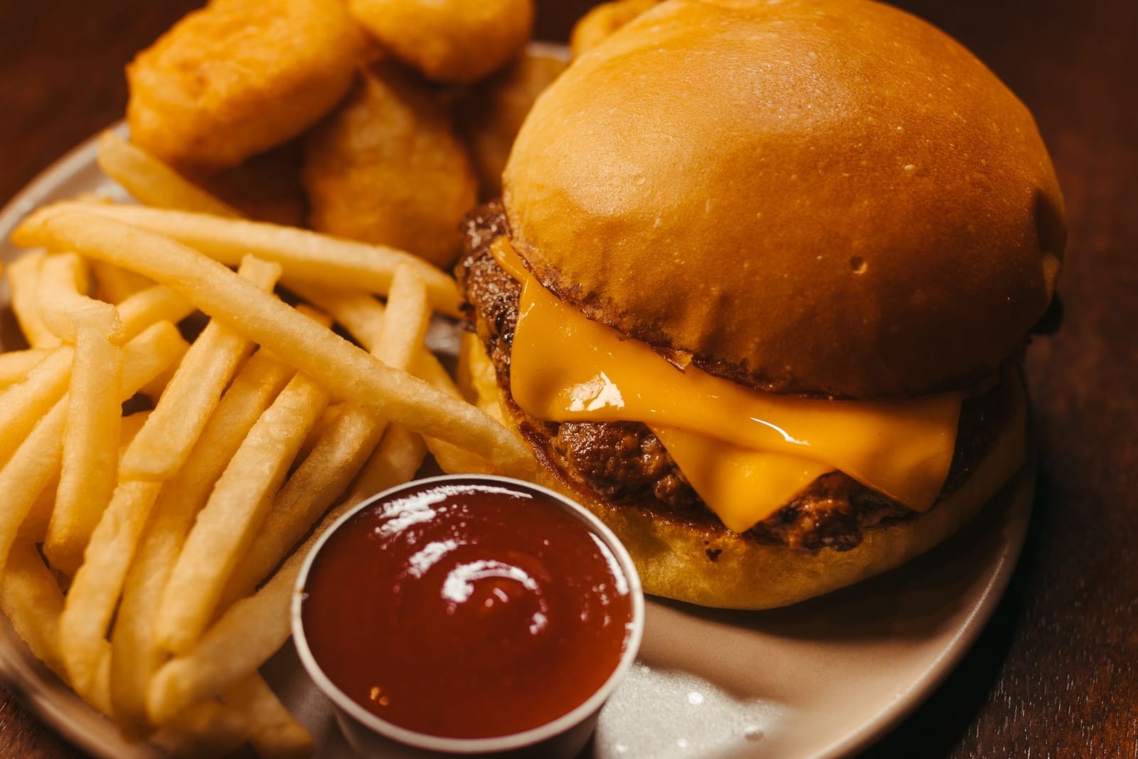 A fast-food cheeseburger with melted cheese, fries and ketchup on a diner plate