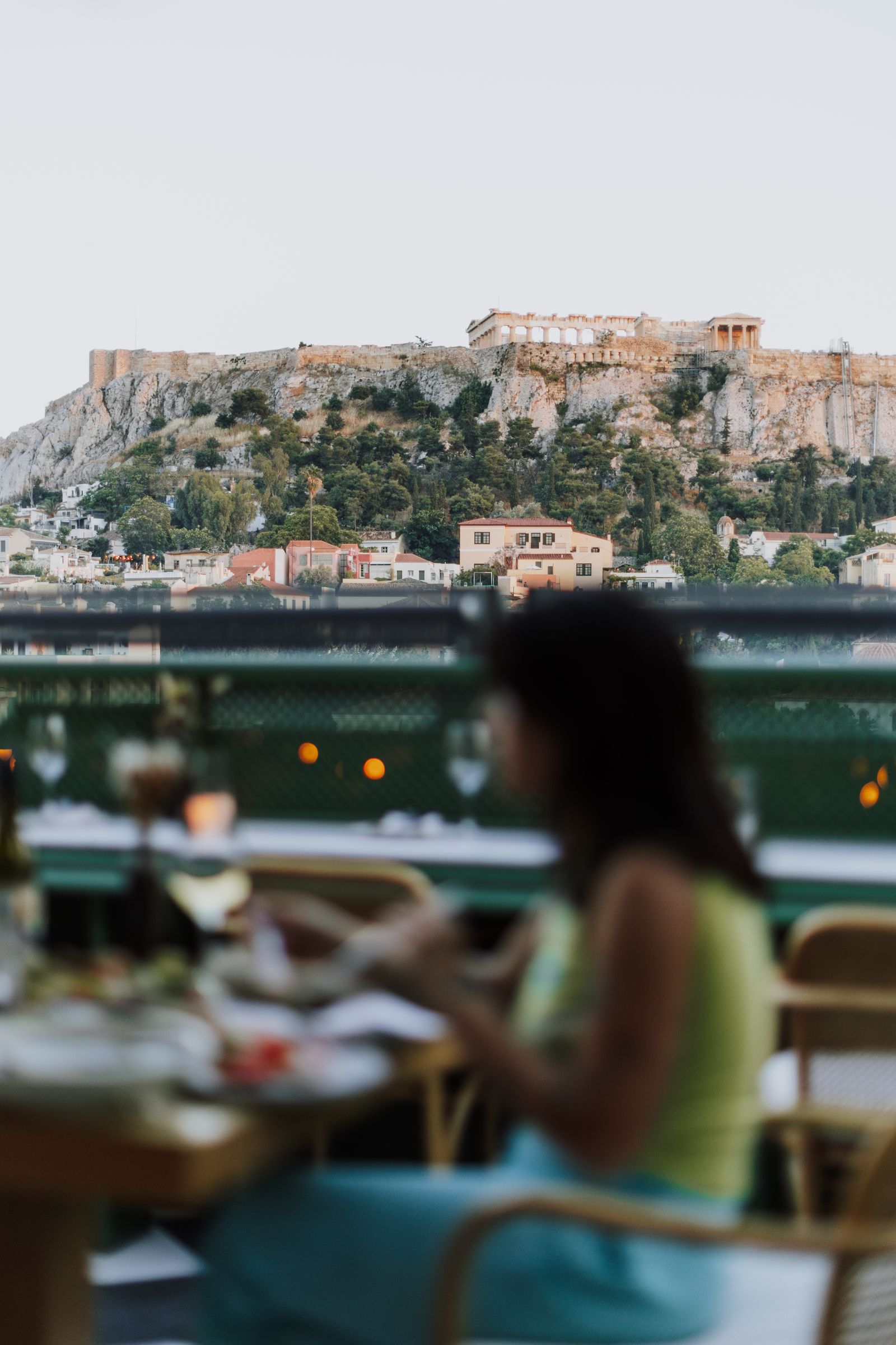 Diners on a rooftop terrace in Athens with the lit Acropolis and Parthenon behind them