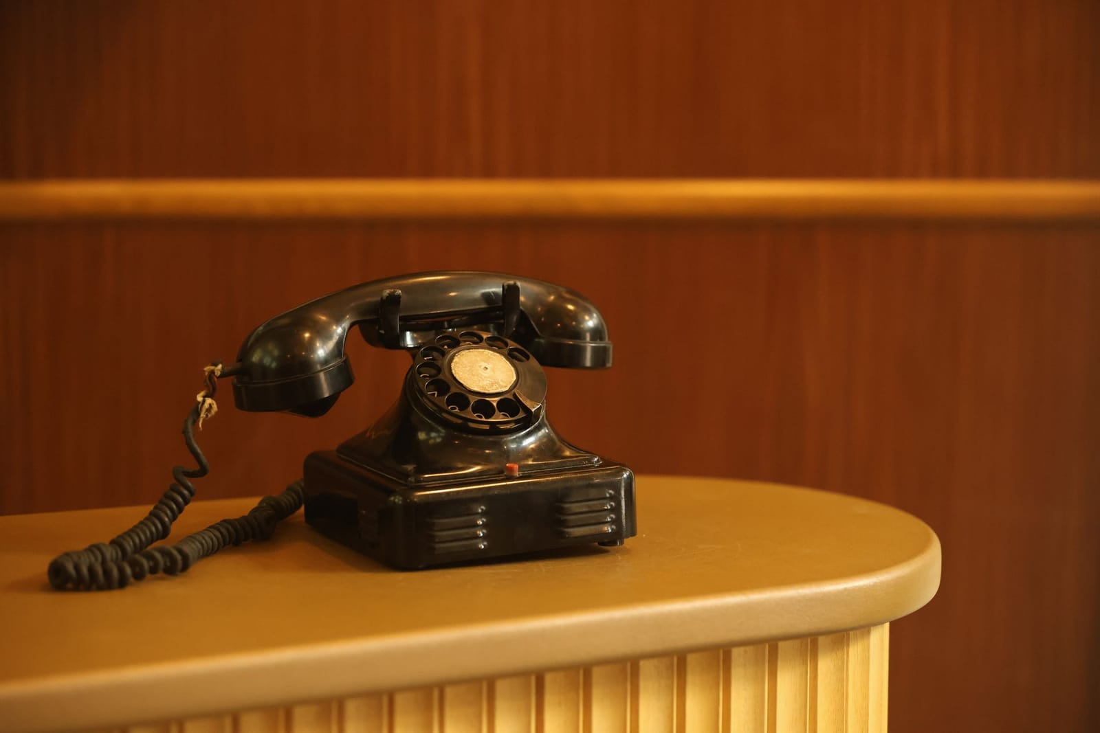 Een zwarte telefoon met draaischijf op een houten receptiebalie