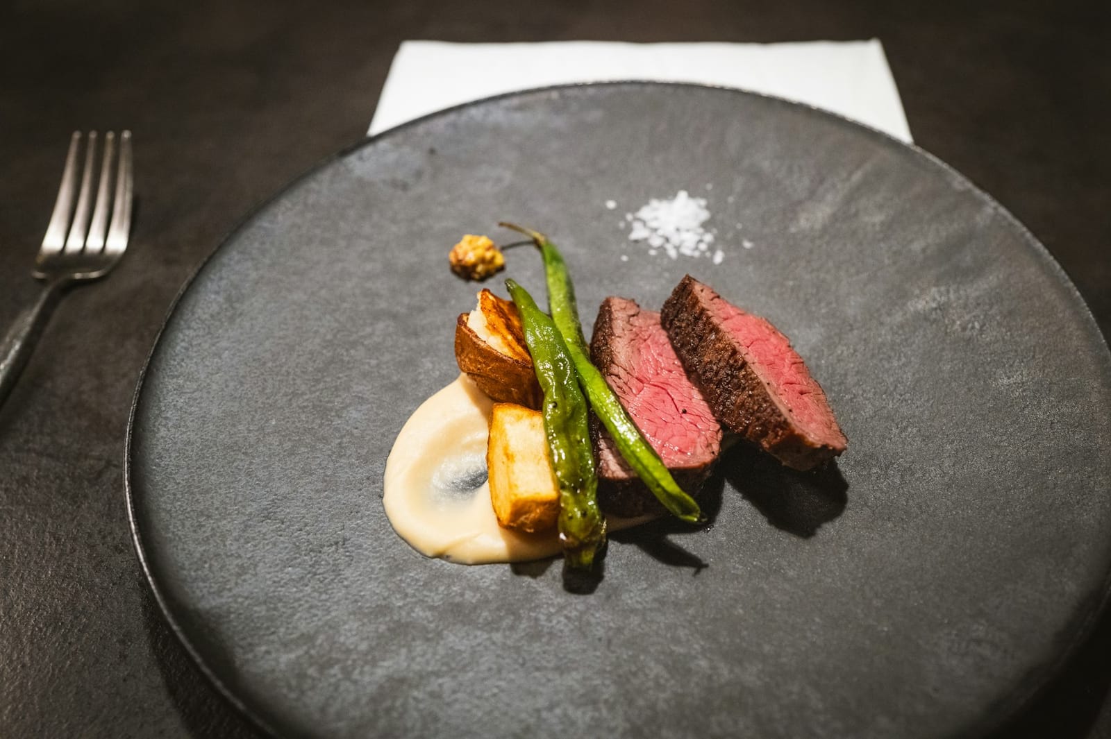 Sliced meat with vegetable puree and green beans on a dark fine-dining plate