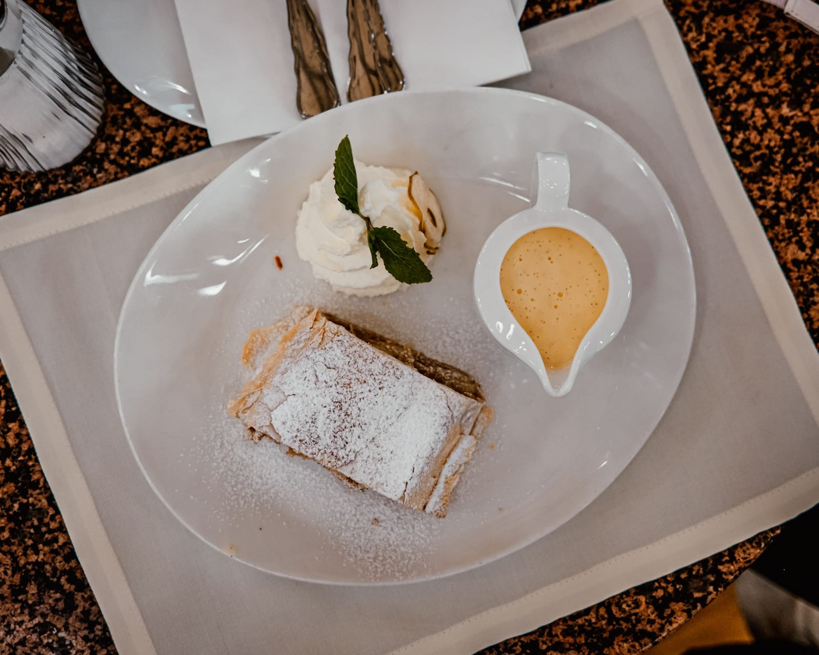 Fetta di strudel di mele con zucchero a velo, panna montata e salsa alla vaniglia