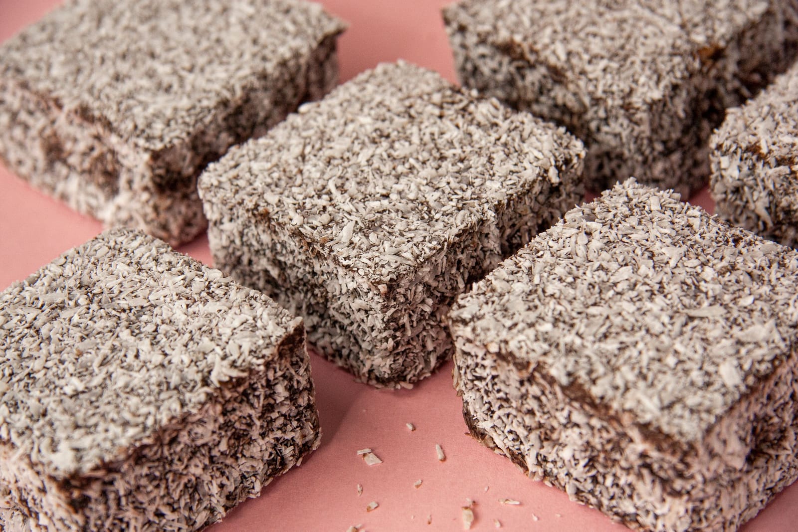 Vierkante lamingtons met chocoladeglazuur en geraspte kokos op een roze ondergrond