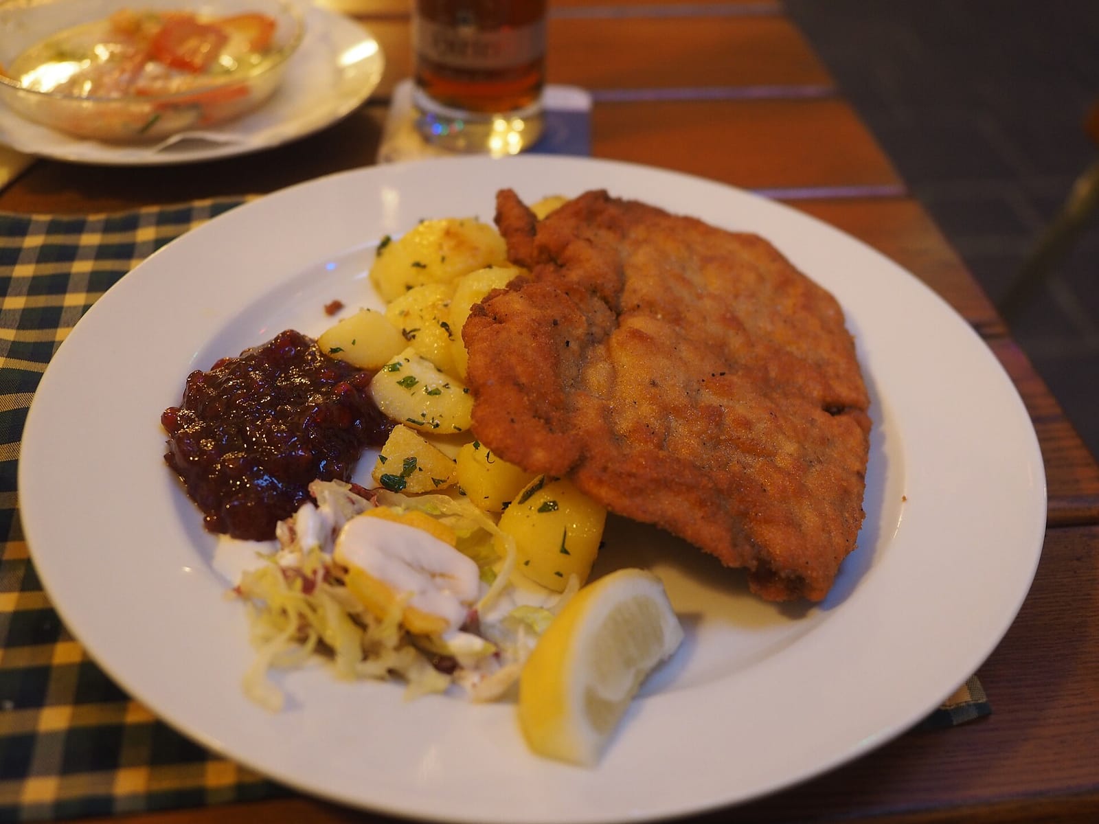 Wiener Schnitzel mit Petersilkartoffeln, Preiselbeeren, Krautsalat und einer Zitronenspalte auf weißem Teller